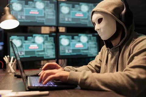 Impostor with mask hacking computer network at night 스톡 사진