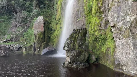 An impressive 90-100 meter waterfall that falls into a dark wine-colored pool Stock Footage 330194063