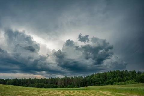 Impressive dark storm clouds are approaching over the forest and the open meadow Stock Photos