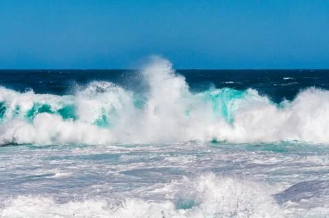 Impressive large ocean wave with white foam against deep blue of ocean and sk Stock Photos
