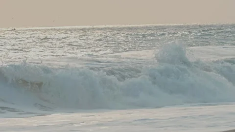 Impressive ocean wave breaking on a sandy beach during a beautiful, hazy sunrise Vídeo Stock 342977369
