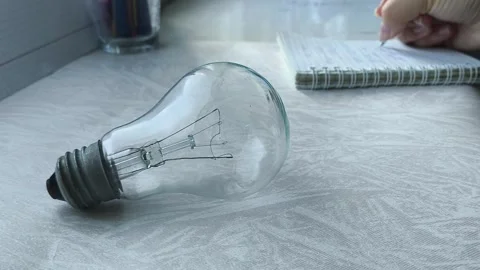 An incandescent lamp is lying on a table, in the background a woman is counting Stock Footage 316286764