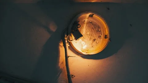 An Incandescent Light Bulb Glows in an Old Broken Lamp on the Concrete Wall Stock Footage 253384986