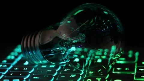 Incandescent light bulb lies on the backlit laptop keyboard at night Stock Footage 291726631