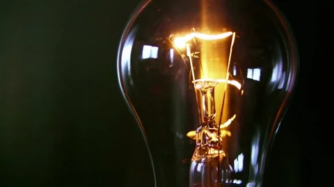 Incandescent light bulb lights up bright on dark background. Stock Footage 340623423