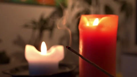 Incense stick smoke rising between two glowing candles Stock Footage 334573139