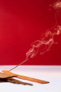 An incense stick smokes on a red background Stock Photos