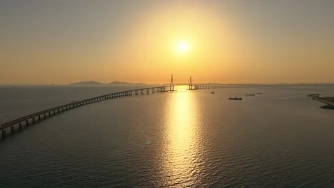 Incheon Bridge silhouette glowing under hazy golden sun with cargo ships passing Stock Footage 340200094