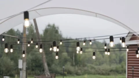 Included string of light bulbs on black wire hangs under the roof of white tent Stock Footage 152328076