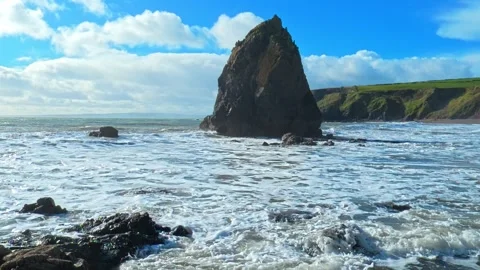 Incoming waves large sea stack drifting clouds in blue sky spring morning Stock Footage 330854499