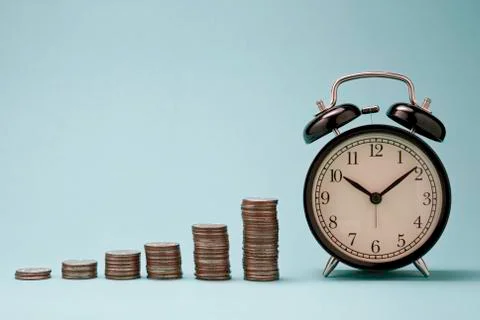 Increase coins stack graph with alarm clock on blue background. Stock Photos