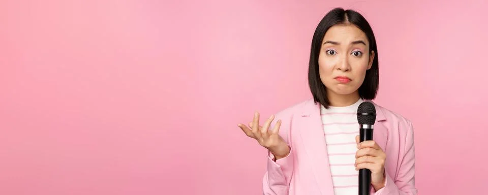 Indecisive, nervous asian business woman holding mic, shrugging and looking Stock Photos