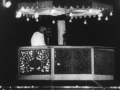 INDIA 1930: Gandhi stands on a canopied stage and speaks into a microphone. Stock Footage
