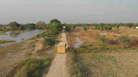 India, A drone camera aerial view of a yellow bus moving on a mud road Stock Footage 109241924