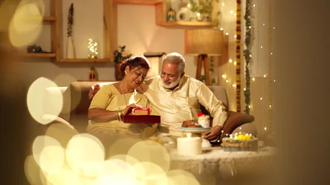 Indian aged couple talking and gave gift,sitting on sofa during diwali. Видео 252591644