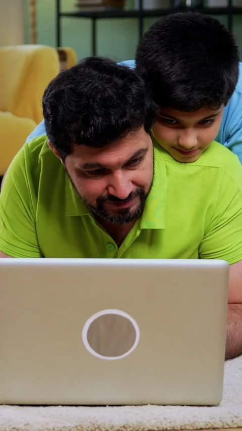 Indian asian man with son using laptop while lying on living room floor at home Stock Footage 342758116