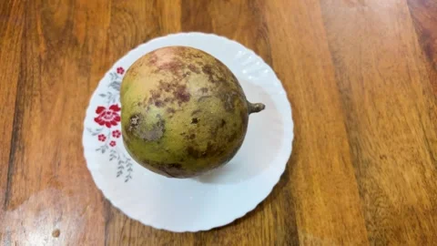 Indian bael fruit whole on white plate with natural wooden surface background Stock Footage 334491640