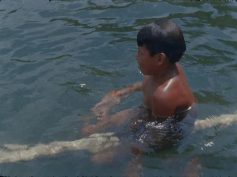 Indian boy on floating log as other children swim and play. Stock Footage 148126306