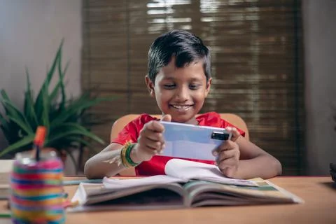 Indian boy taking notes while studying online with a teacher at home. And kee Stock Photos