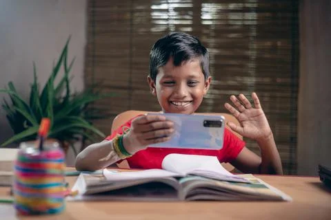Indian boy taking notes while studying online with a teacher at home. And kee Fotos Stock
