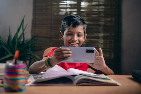 Indian boy taking notes while studying online with a teacher at home. And kee Fotos Stock