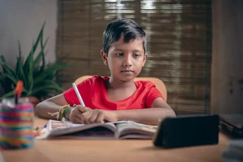 Indian boy taking notes while studying online with a teacher at home. And kee Stock Photos