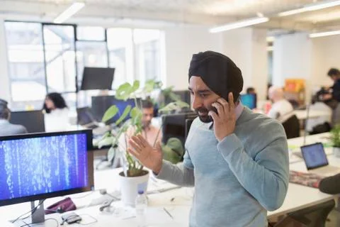Indian computer programmer in turban talking on smart phone in office 写真素材