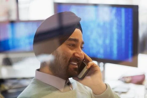 Indian computer programmer in turban talking on smart phone in office Foto stock