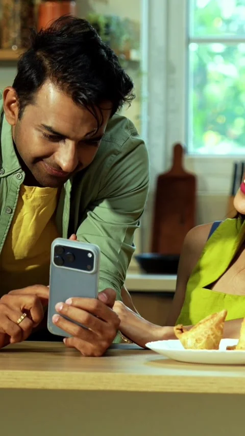 Indian couple surfing internet checking photos on smartphone in kitchen Stock Footage 342689055