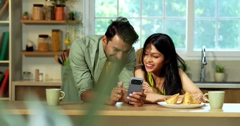 Indian couple surfing internet checking photos on smartphone in kitchen Stock Footage 342691004