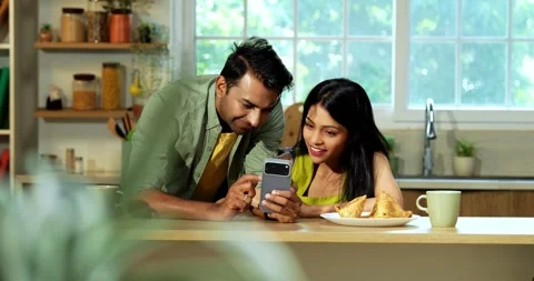 Indian couple surfing internet checking photos on smartphone in kitchen Stock Footage 342691096