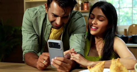 Indian couple surfing internet checking photos on smartphone in kitchen Stock Footage 342691196