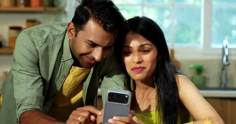 Indian couple surfing internet checking photos on smartphone in kitchen Stock-Footage 342691214