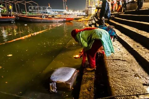 Indian devotee offering oil lamp to holy river ganges at evening from flat 写真素材