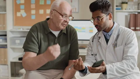 Indian Doctor Explaining Diabetes App on Smartphone to Senior Man Stock Footage 339629418