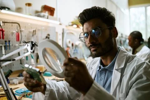 Indian Engineer Inspecting Circuit Board with Magnifier in Tech Lab 写真素材