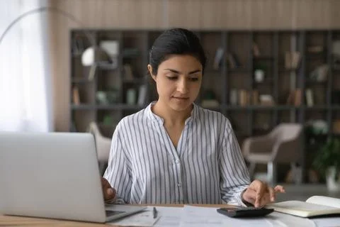 Indian female auditor prepare analytic report using laptop handheld calculator Stock Photos