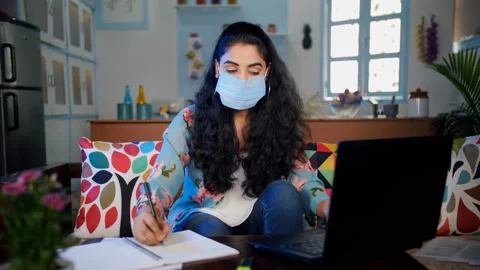 Indian female making notes of her online education wearing a medical mask Stock Footage 145790197