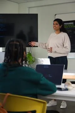 Indian female presenter gesturing, showing code on screen with laptop in Stock Photos