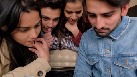 Indian friends focused and transfixed to a portable handheld electronic device t Stock Footage 101233132