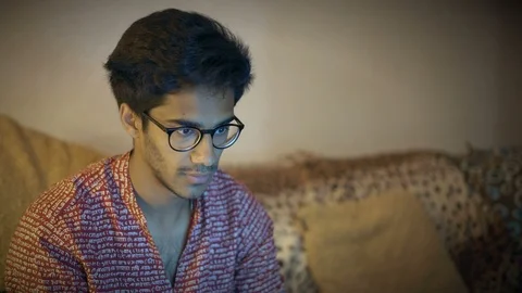 Indian Guy In Glasses Sits On Sofa And Looks At Laptop Monitor Screen Stock Footage 90861473