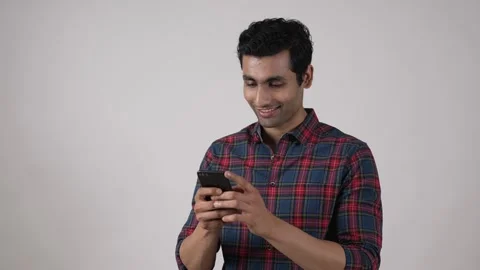 Indian guy typing message on his smart phone while standing in studio. Видео 169908874
