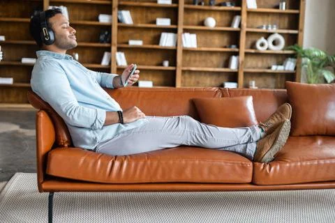 Indian guy using smartphone and wireless headphones for listening music Stock Photos