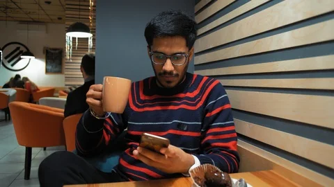 Indian Guy Writes a Message on a Smartphone with a Cup of Coffee in Cafe Stock Footage 101650900