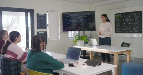 Indian instructor in diverse class starting, presenting code on TV, pointing to Stock Footage 340810949