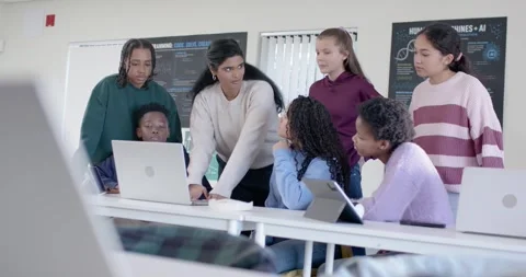 Indian instructor leaning and pointing at laptop at table, guiding teens using Stock Footage 341028914