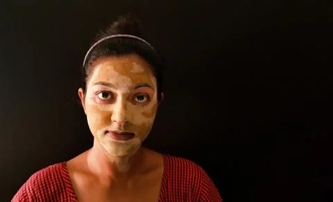 An indian lady with face pack applied in half dried condition staring at came Stock Photos