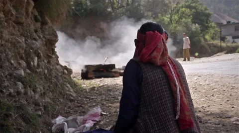 Indian lady sitting next to burning wood and cyclist passing in the background Stockbeeldmateriaal 45312962