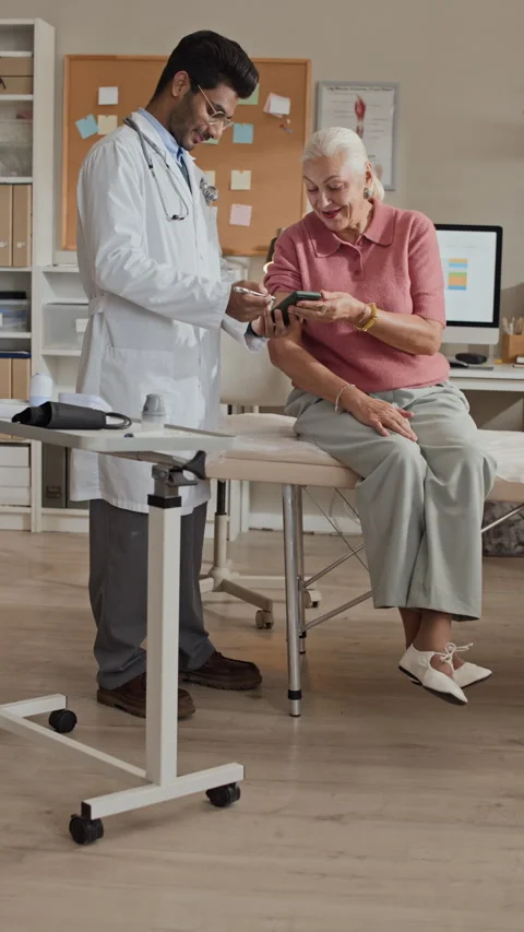 Indian Male Doctor Explaining Mobile App to Senior Female Patient Stock Footage 339624322