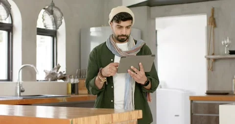 Indian man behind kitchen island holding tablet, tapping screen, nodding and Stock Footage 341240946
